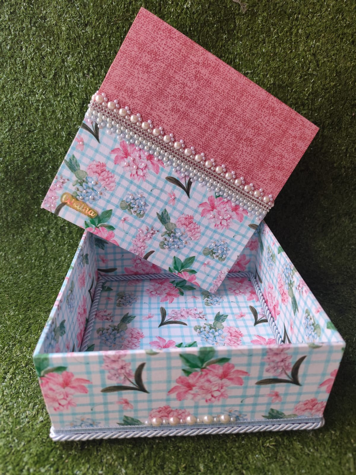 Caixa decorada aberta com estampa floral, tampa rosa, nome Cristina e acabamento de pérolas e cordão